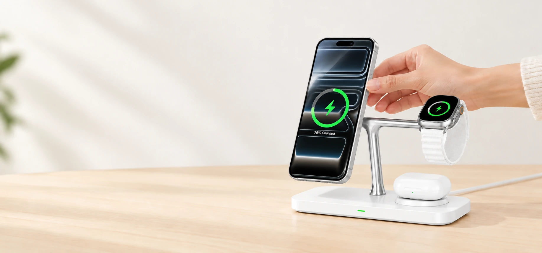 Hand placing a phone on the left charging head of a white chrome dock, with watch and earbuds on their original pads.