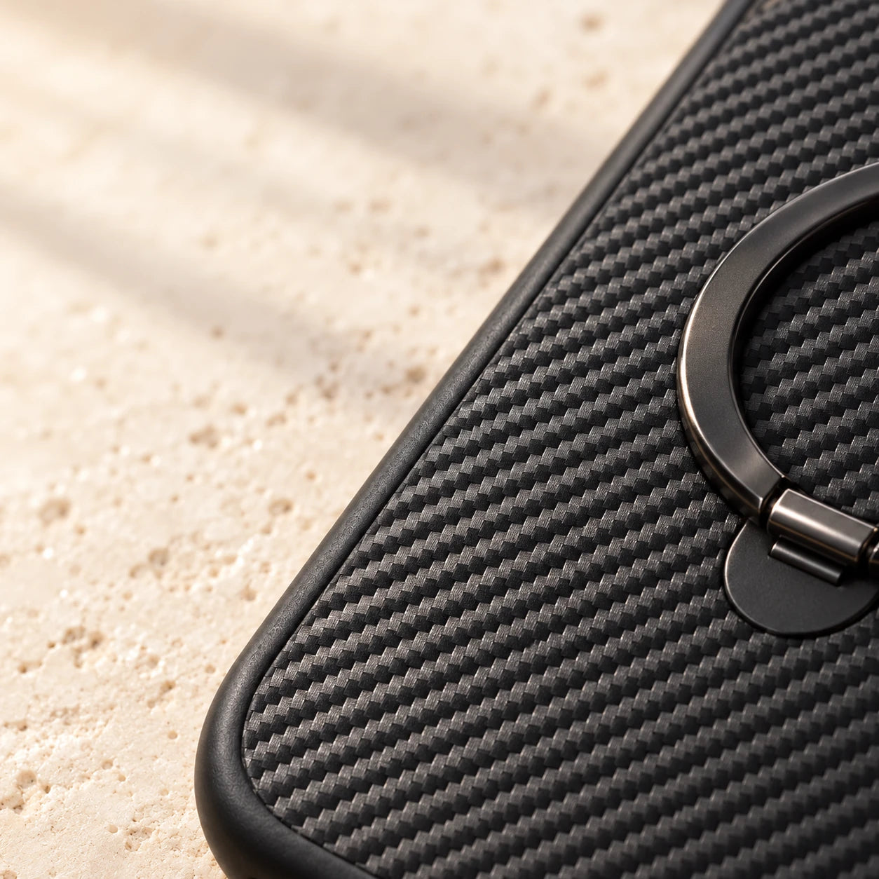 Close-up of diagonal carbon-pattern texture and the folded black ring on a phone case.
