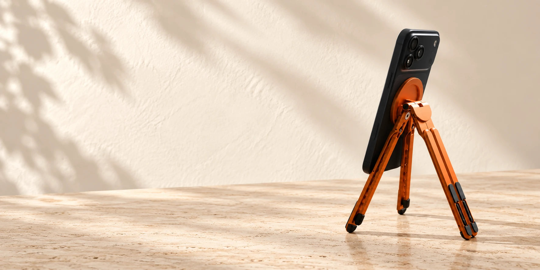 Orange folding magnetic stand supporting a black phone on a desk.